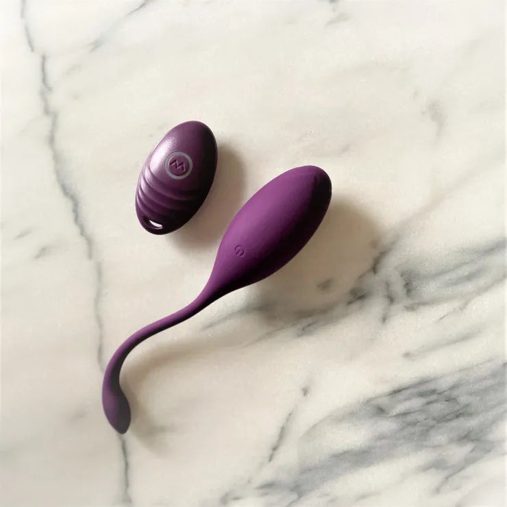 Paars vibrerend ei met flexibel staartje en bijpassende draadloze afstandsbediening op marmeren ondergrond