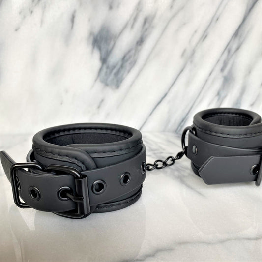 Zwarte vegan leren handboeien close-up met gesp, ketting en zachte voering op marmer